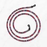 Correa para lentes trenzada con patrón multicolor en tonos rojos, azules y blancos, con terminales de goma negra y detalles metálicos plateados.