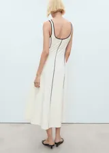 Vestido midi color crudo con tirantes anchos y escote cuadrado. Presenta ribetes negros en cuello, sisas y costuras verticales.
