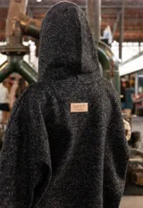 Campera tipo overshirt de paño jaspeado en color negro, con calce oversize, capucha y cordones trenzados. Presenta un diseño versátil con interior suave y abrigado.