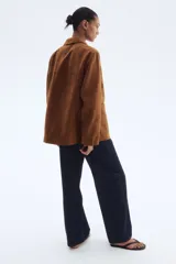 Campera marrón de tejido suave con acabado cepillado, estilo chaqueta o saco. Presenta solapas de muesca, cierre frontal de tres botones y dos bolsillos parche grandes en la parte delantera inferior.