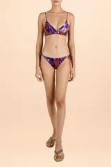 Bombacha de bikini con estampado de hojas en tonos púrpura y cobre, con tiritas laterales ajustables y ribetes decorativos.