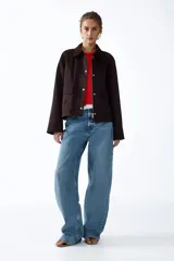 Campera de sarga color marrón oscuro, con cuello camisero de pana, cierre frontal oculto por solapa con botones a presión y bolsillos frontales grandes con solapa.