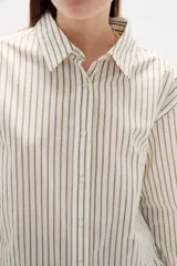 Camisa de algodón con diseño de rayas verticales finas en tonos neutros, corte holgado, cuello camisero y cierre frontal con botones.