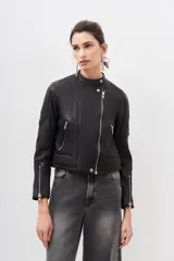 Campera de cuero ovino color negro, con cierre frontal asimétrico, cuello redondo con broche a presión y cierres metálicos en los puños.