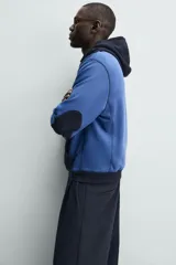 Sudadera hoodie regular fit de color azul, con capucha y bolsillo canguro negro. Cuenta con cordones ajustables blancos y detalles en color negro en la capucha, el bolsillo y los puños.