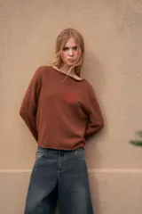 Sweater de punto liviano color beige, con cuello bote, mangas largas y detalle de bordado en el pecho.
