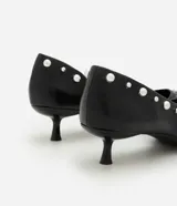 Zapato estilo kitten heel de cuero sintético negro, con punta fina y aplicación de pequeñas tachas metálicas a lo largo del borde superior.