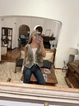 Chaleco marrón de corte corto con bordados florales en color crema en el frente y cierre frontal con botones. Presenta un diseño estructurado con cuello camisero.