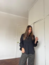 Camisa negra de corte peplum con detalles de bordado inglés en el pecho, cuello redondo y mangas largas con puños acampanados.