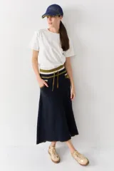 Falda midi de lana en color marrón, con diseño acampanado y tejido acanalado. Presenta una cintura elástica con cordón de ajuste, detalles de rayas en tonos beige y blanco en la parte superior, y costuras decorativas en el ruedo.