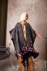 Poncho tipo ruana tejido en telar artesanal, color negro con textura de puntos blancos y decorado con pompones multicolores y flecos largos en los bordes.