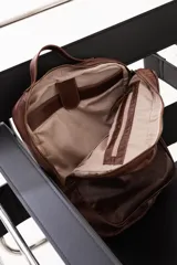Mochila de cuero genuino color marrón, con diseño minimalista, compartimento principal con cierre, bolsillo frontal con etiqueta de marca y correas ajustables.