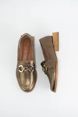 Mocasines de cuero en tono bronce metalizado, con detalle de aplique metálico dorado en el empeine y taco cuadrado bajo de madera.