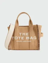 Cartera tipo tote bag de lona color beige, con diseño estructurado y asas superiores. Presenta el logo de la marca estampado en la parte frontal y detalles de cintas laterales con inscripciones.