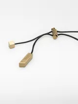 Collar de cordón negro regulable con un dije metálico irregular de color dorado y terminales logotipados.