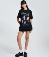 Remera negra de algodón con cuello redondo y mangas cortas. Presenta un estampado gráfico frontal con imágenes de Chuck Bass de la serie Gossip Girl y lettering decorativo.