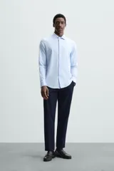 Camisa de manga larga, color celeste con finas rayas verticales blancas, cuello italiano y cierre frontal de botones.