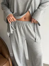 Conjunto de dos piezas color gris melange, confeccionado en tela de lanilla, compuesto por un buzo de manga larga con diseño cruzado al frente y un pantalón largo de corte holgado y tiro alto.