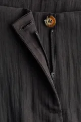 Pantalón tobillero negro de tejido arrugado, con cintura de tiro alto, pliegues delanteros y corte holgado de piernas barrel con elástico y cordón ajustable en los tobillos.