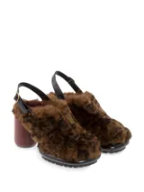 Sueco negro con pelo sintético, taco de madera y hebilla trasera para ajustar al talón.