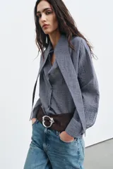 Cinturón ancho de ante color marrón con hebilla metálica plateada de diseño orgánico y forma ovalada.