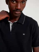 Chomba de manga corta color negro con cuello y tapeta interior en color gris claro. Presenta un pequeño bordado en el pecho y detalles de ribete en gris en el cuello y las mangas.