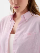 Camisa de corte clásico con cierre frontal de botones, cuello camisero, manga larga con puños abotonados y un bolsillo en el pecho con el logo de la marca bordado. Presenta un diseño de rayas verticales finas en tono rosado.