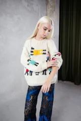 Sweater de lana tejido y bordado a mano, de color crudo con diseño de figuras coloridas. Presenta un calce holgado, cuello redondo y mangas largas.
