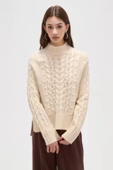 Polera de tejido de punto color crema, con cuello alto y diseño de trenzas verticales. Presenta mangas largas con puños acanalados y un corte holgado.