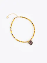 Collar corto elaborado con mostacillas de vidrio en tonos amarillos y marrones, con un dije central metálico en forma de vaquita de San Antonio color bordó. Incluye cadena de extensión para regular el largo.