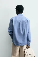 Camisa de hombre de manga larga, color azul, con cuello solapa y bolsillo plastrón en el pecho. Presenta un patrón de cuadros pequeños en tonos de azul y blanco.