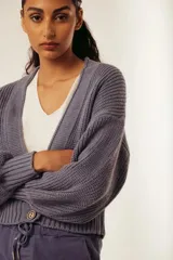 Saco de tejido de punto grueso color gris azulado, con cuello en V y manga larga abullonada. Presenta un solo botón de madera en la parte inferior delantera.