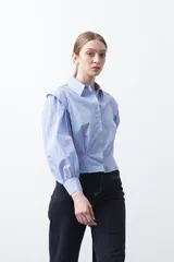 Camisa a rayas azules y blancas de manga larga, con cuello clásico y puños abotonados. Presenta un diseño entallado en la cintura.