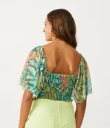 Blusa cropped de tul con estampado de bananas, escote cuadrado, mangas cortas amplias, detalle de látex en el cuerpo y volantes en el bajo.