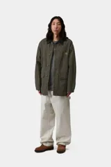 Campera de gabardina Carhartt WIP modelo Prescott, color verde militar, con cuello camisero de pana negra contrastante, cierre frontal de botones y bolsillos frontales amplios. Cuenta con detalle de logo bordado en el pecho.