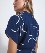Mono largo Marfinno de color azul marino con estampa geométrica en color blanco, de corte estilo aladín con mangas cortas, cuello camisero, cierre frontal con botones y puños ajustados en los tobillos. Incluye un cinturón de cuerda ajustable en la cintura con nudos y detalles de esferas en las puntas.