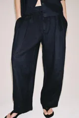 Pantalón de tiro medio confeccionado en 100% lino, color blanco, de corte amplio y recto. Cuenta con cintura elástica posterior, trabillas, pinzas en el delantero, bolsillos laterales y cierre frontal con cremallera y botón oculto.
