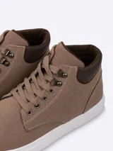 Bota urbana de caña media confeccionada en gamuza color marrón, con cuello acolchado en contraste, sistema de cordones con ojalillos metálicos y suela plana blanca.