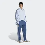 Pantalón deportivo Adidas de corte clásico, color azul con las icónicas tres tiras blancas laterales. Presenta el logo del Trifolio bordado en la parte superior y cordón de ajuste en la cintura.