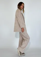 Blazer de lino y algodón en tono beige con textura a rayas verticales sutiles. Presenta solapas clásicas, un solo botón frontal marrón y un corte ligeramente holgado. Los bordes de las mangas y el ruedo tienen un acabado deshilachado.