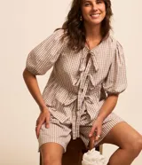 Blusa Marfinno confeccionada en tricolina de algodón con estampado de cuadros vichy, de manga corta abullonada, cuello redondo, abertura frontal con lazos y recorte fruncido en la cintura.