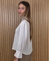 Blusa blanca de algodón con escote en V y cuello mao. Presenta mangas largas abullonadas con puños acampanados y fruncidos.