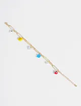 Pulsera dorada con cadena de eslabones rectangulares y dijes colgantes de plástico y vidrio: cara sonriente amarilla, ojo turco azul, ojo turco rojo, perla blanca y fantasma blanco.