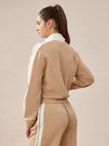 Campera deportiva tostada con cierre frontal blanco, cuello alto y bandas blancas en las mangas.