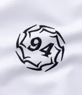 Remera de manga corta en tejido sintético color blanco, con cuello redondo y diseño de estilo deportivo. Presenta estampado frontal con lettering gótico y detalles laterales en tejido microperforado.