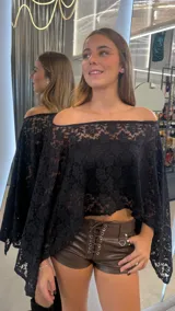 Top tipo capa confeccionado en encaje negro con diseño floral. Presenta un corte holgado, escote estilo hombros caídos y mangas amplias.