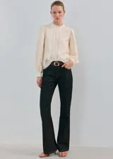 Blusa de color crema con cuello redondo, mangas largas abullonadas y detalles de bordado y puntilla vertical en el frente.