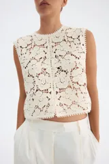 Chaleco sin mangas de punto crochet color crema, con diseño floral calado y ribetes de picot en cuello, sisas y ruedo. Cierre frontal con botones nacarados.