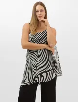 Enterito de seda fría con pantalón palazzo de corte ancho y fluido. Presenta un diseño asimétrico con una tira fina en un hombro y un detalle de herraje metálico en el otro, del cual se desprende una capa de gasa estampada con patrón abstracto en blanco y negro.