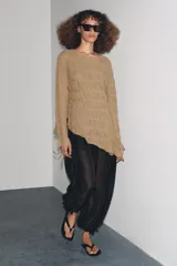 Top de manga larga color beige, con textura fruncida en todo el cuerpo y mangas. Presenta cuello redondo y bajo asimétrico con aberturas laterales ajustables con cordones.